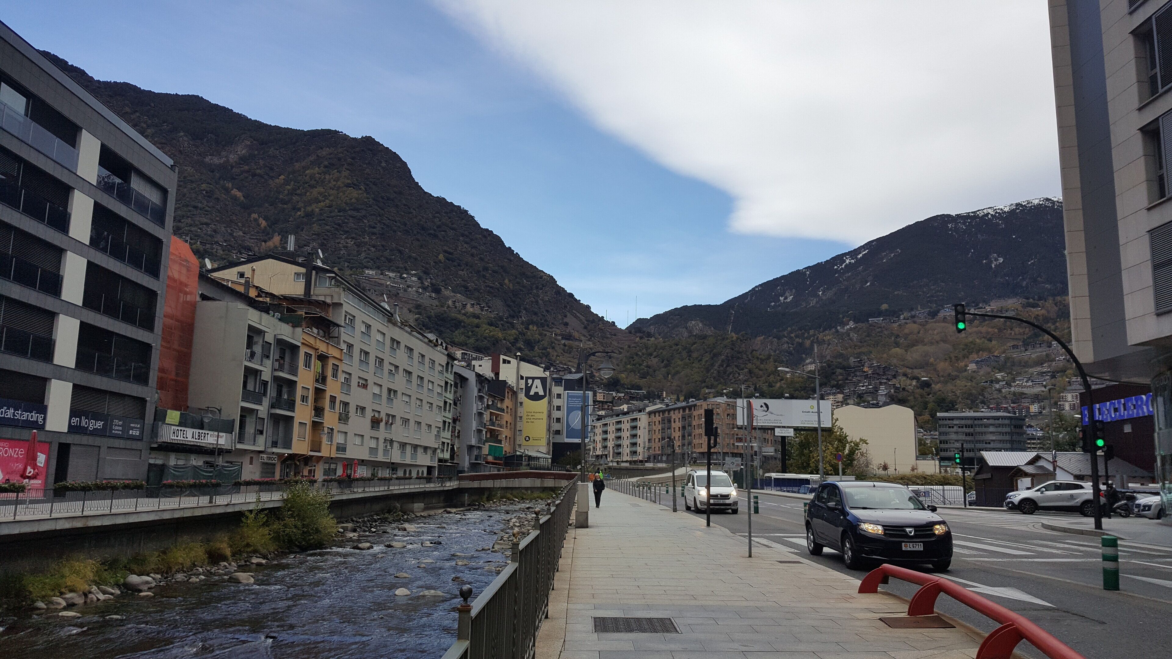 A riverside walkway with buildings, a pedestrian, and cars.