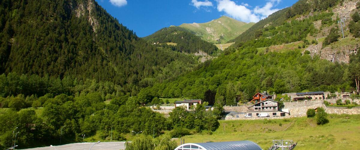 A mountainous landscape with dense forests, a clear blue sky, and several buildings nestled among the hills.