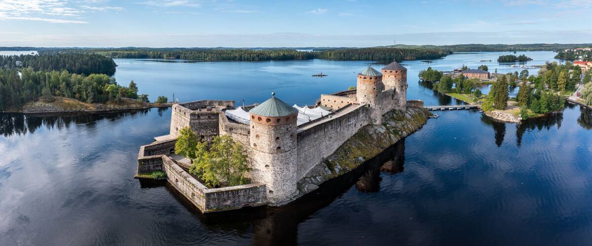 A medieval castle on a lake island surrounded by calm waters and forested land.