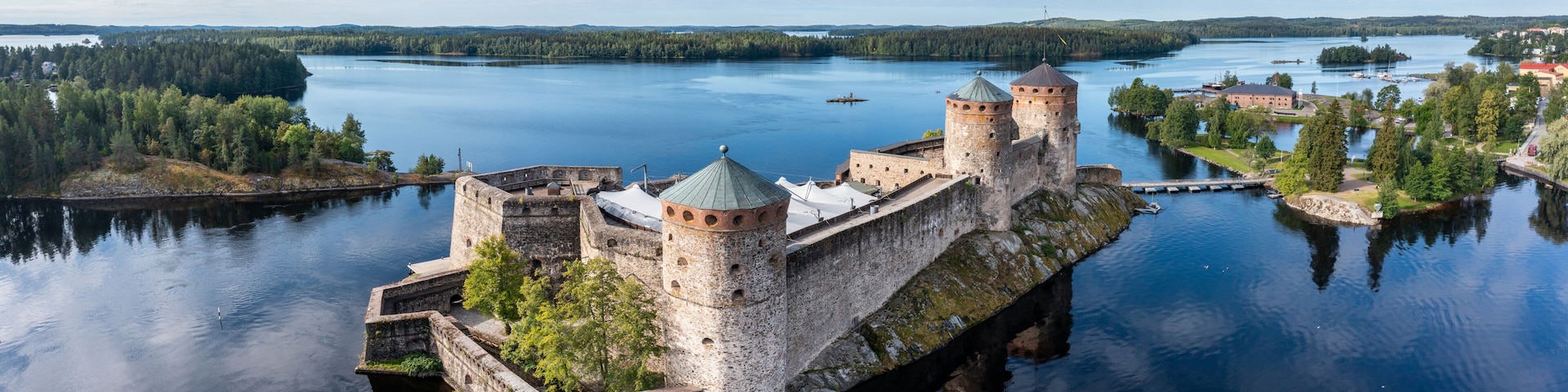 A medieval castle on a lake island surrounded by calm waters and forested land.