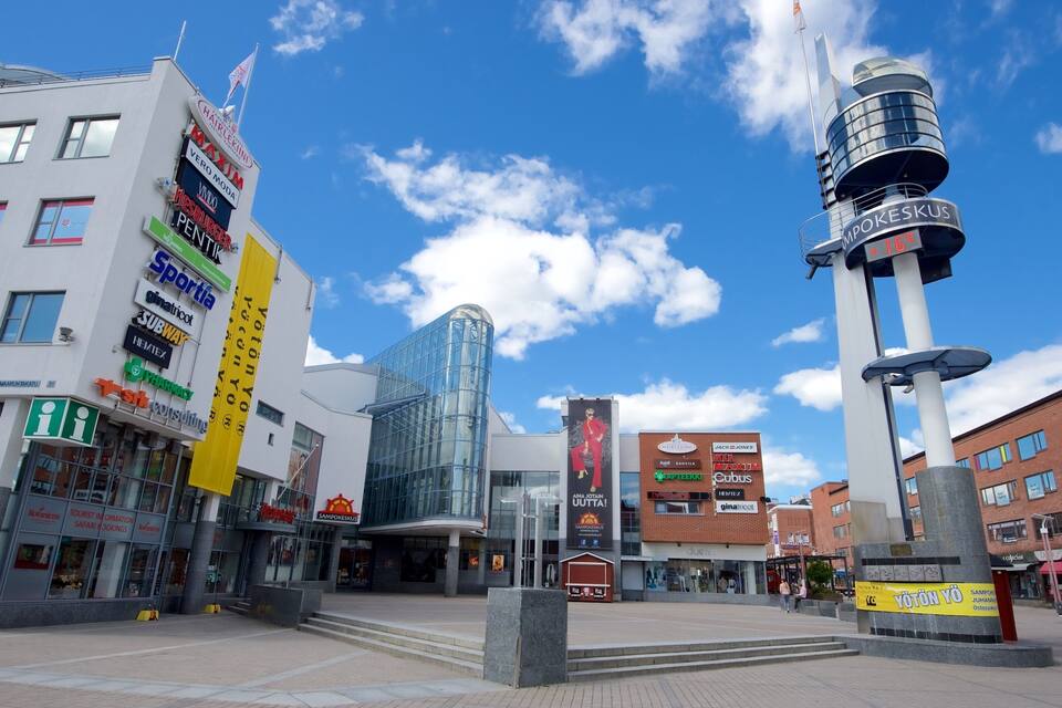 Ein moderner Stadtplatz mit verschiedenen Geschäften, einem hohen Aussichtsturm und blauem Himmel.