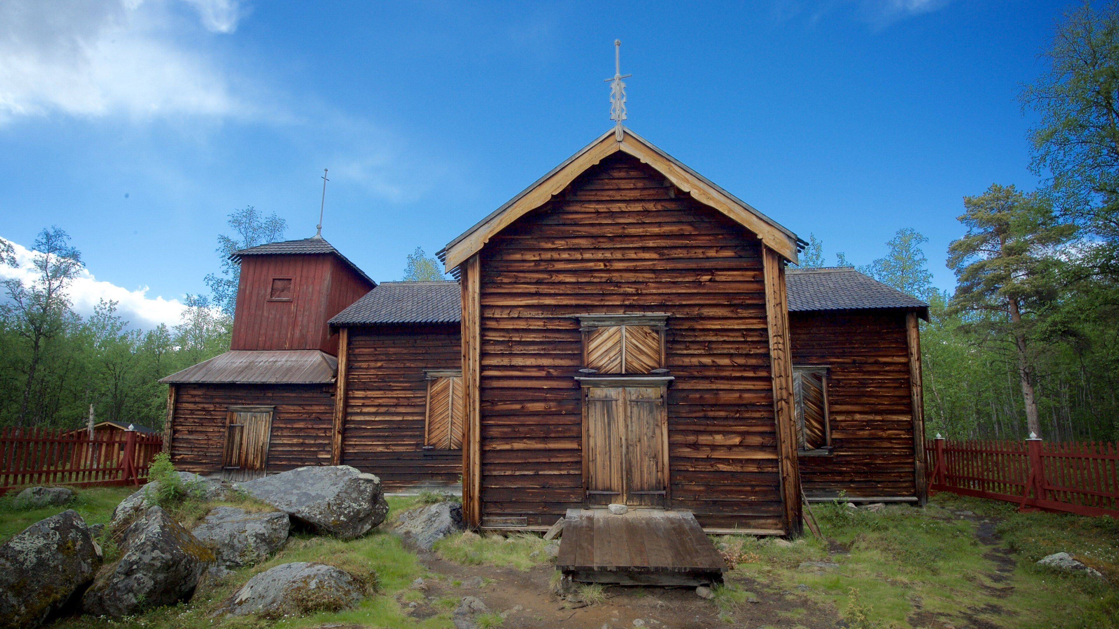 Una iglesia de madera con un campanario y una cerca de madera.