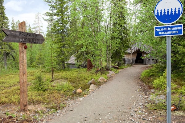 A forest path leading to a cabin with a sign indicating directions to Varkankurun and Vellhopullee.