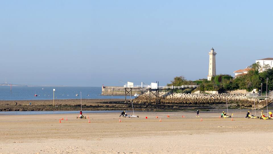 A beach with a lighthouse, rocky shoreline, and a building with a red roof.