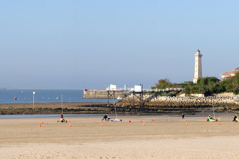 A beach with a lighthouse, rocky shoreline, and a building with a red roof.