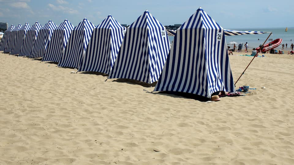 A beach with striped beach umbrellas and a red slide.