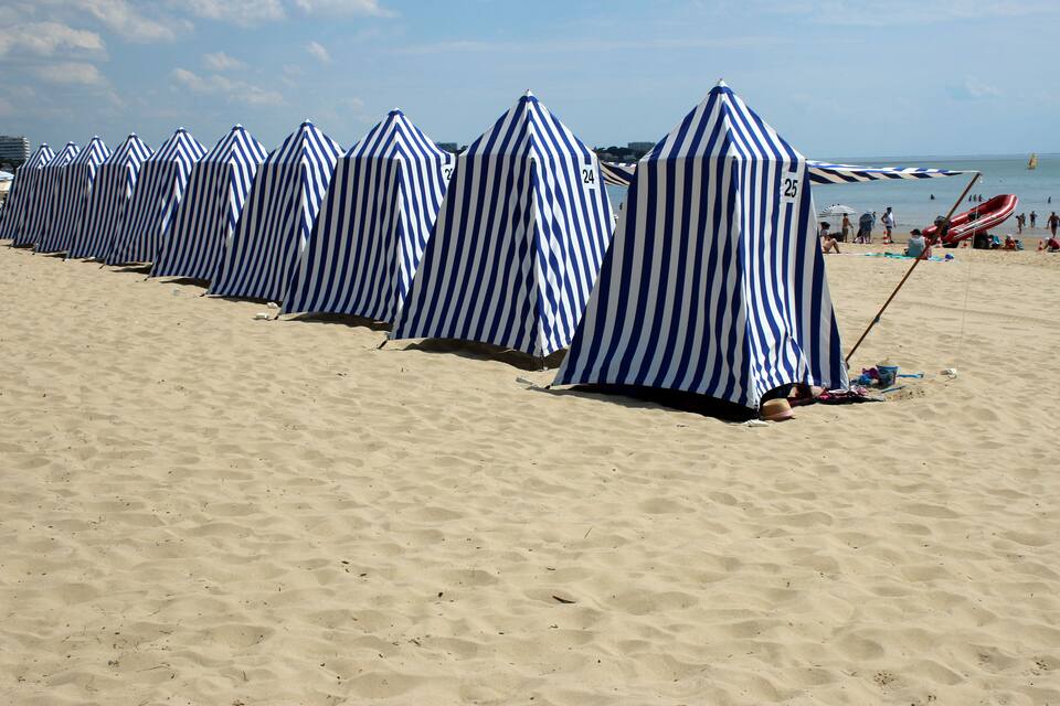 A beach with striped beach umbrellas and a red slide.