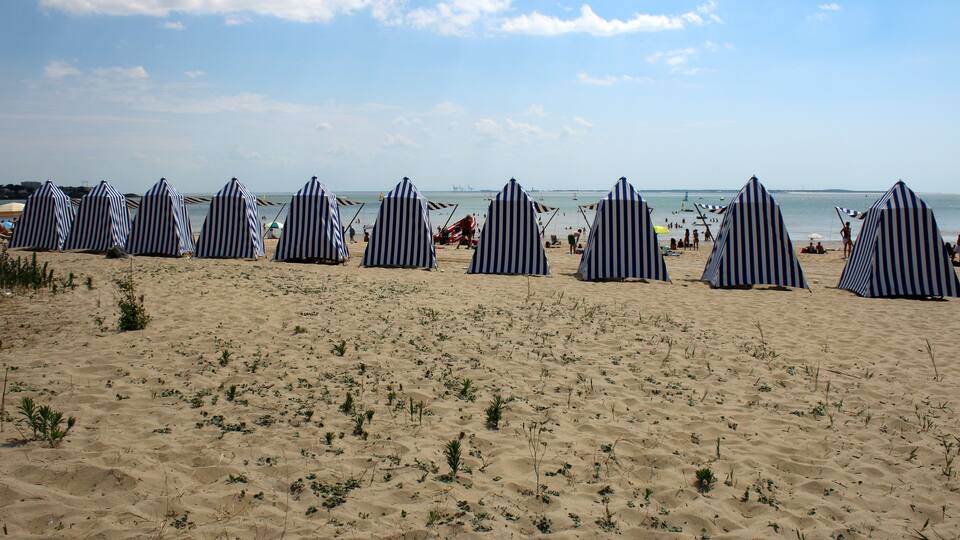 A beach with striped beach umbrellas and sparse vegetation.
