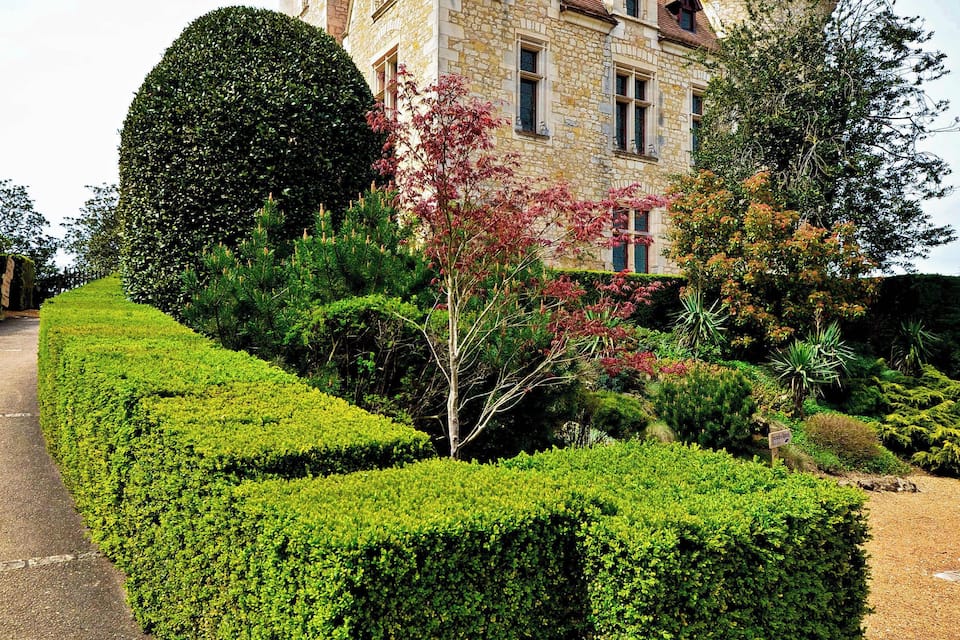 A castle with a round tower, a well-manicured garden, and a paved pathway.