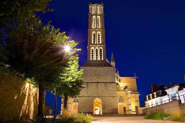 Uma igreja em estilo gótico com uma torre alta, janelas iluminadas e uma entrada arqueada.