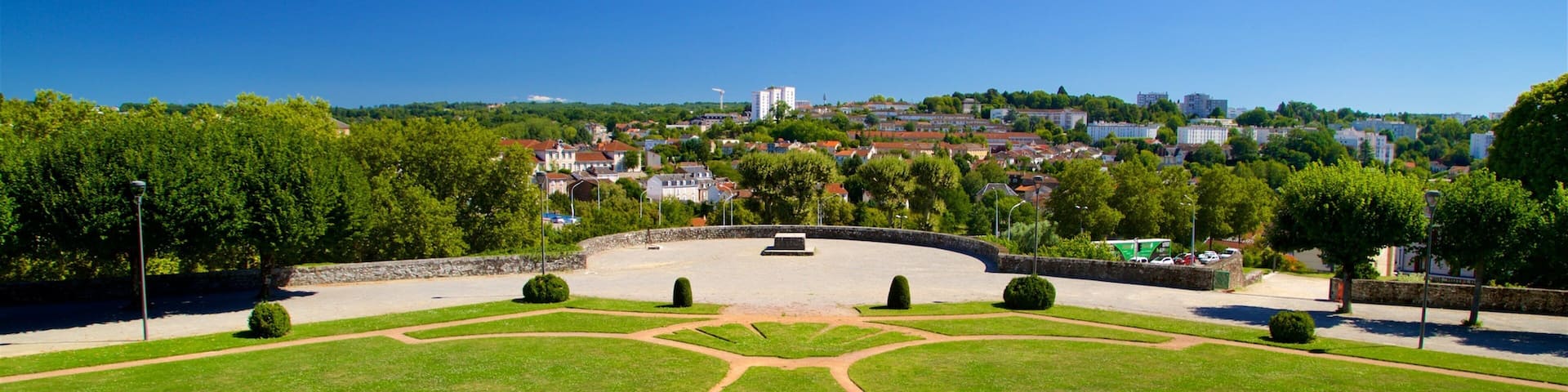 A park with a circular lawn and a monument in the center, surrounded by trees and buildings in the background.
