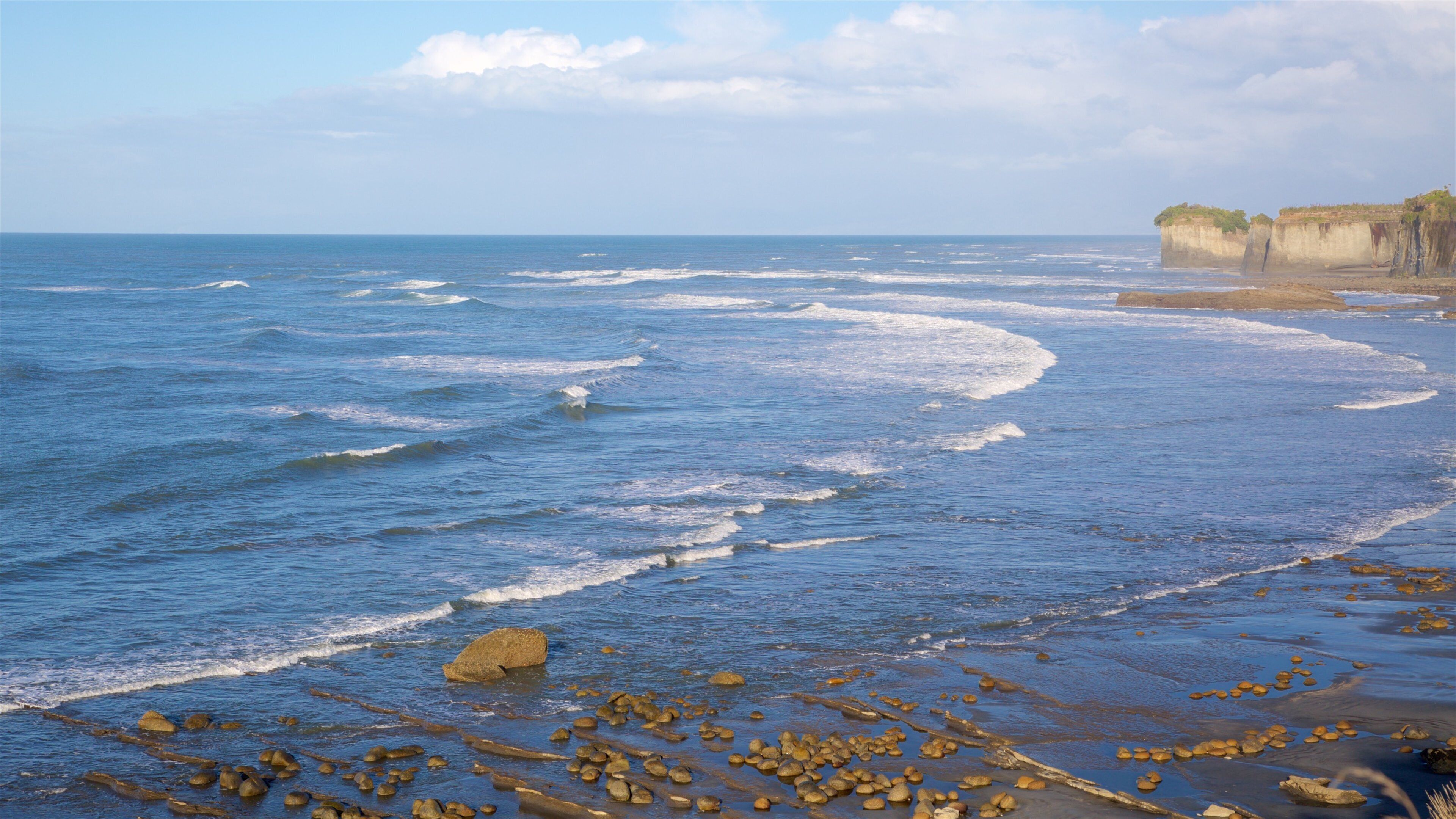 A beach with waves, rocks, and cliffs.