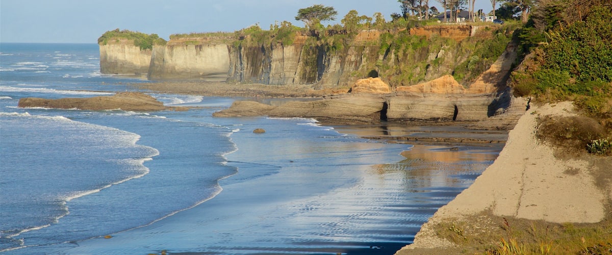 A coastal landscape with cliffs, a sandy beach, and sparse vegetation.