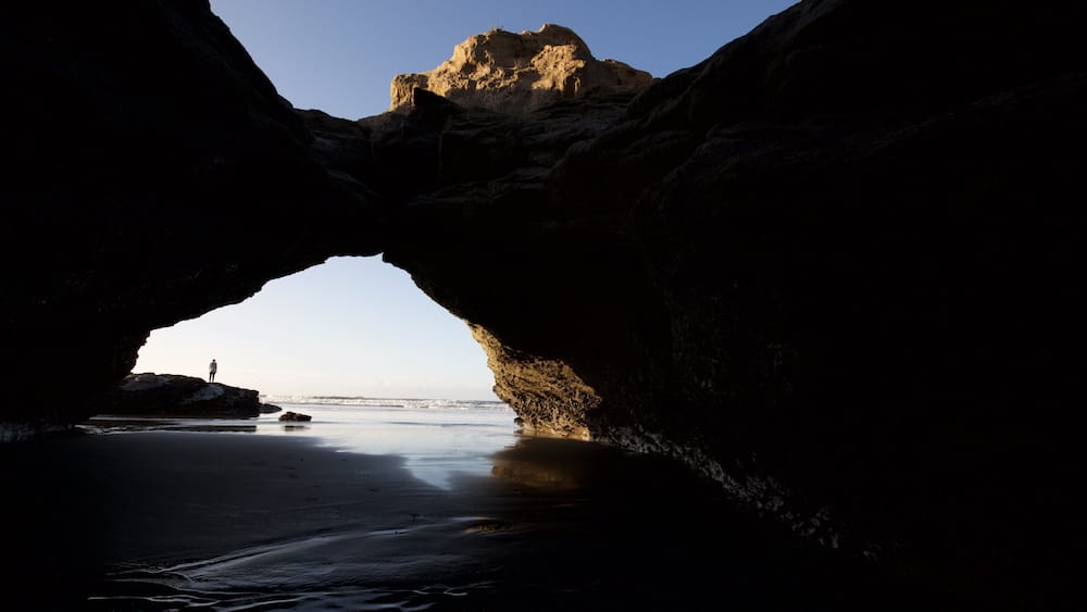 Formação natural de arco de pedra com uma pessoa em sua base.