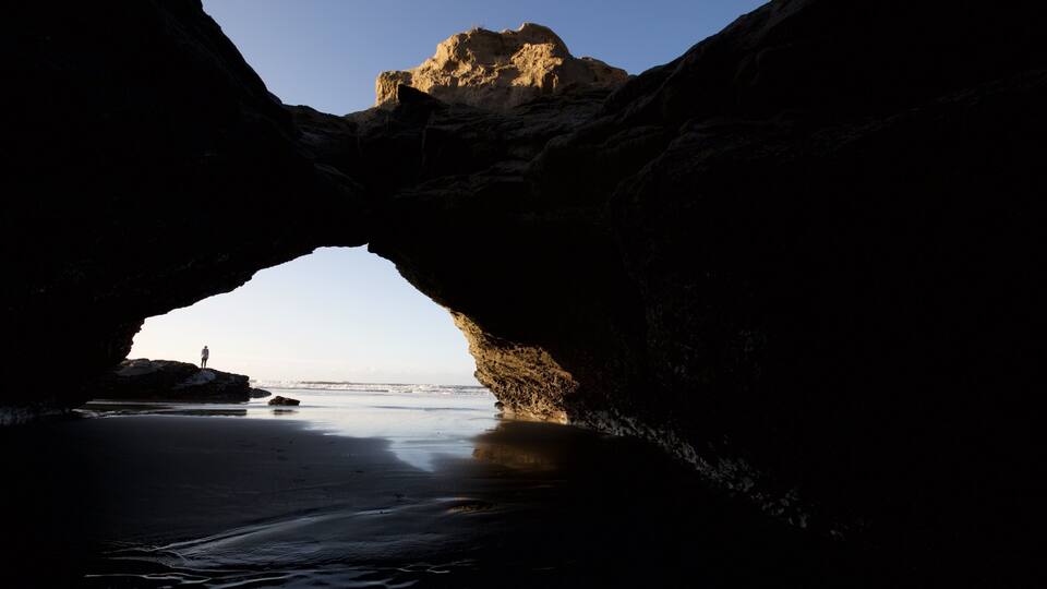 A natural rock arch formation with a person standing at the base.