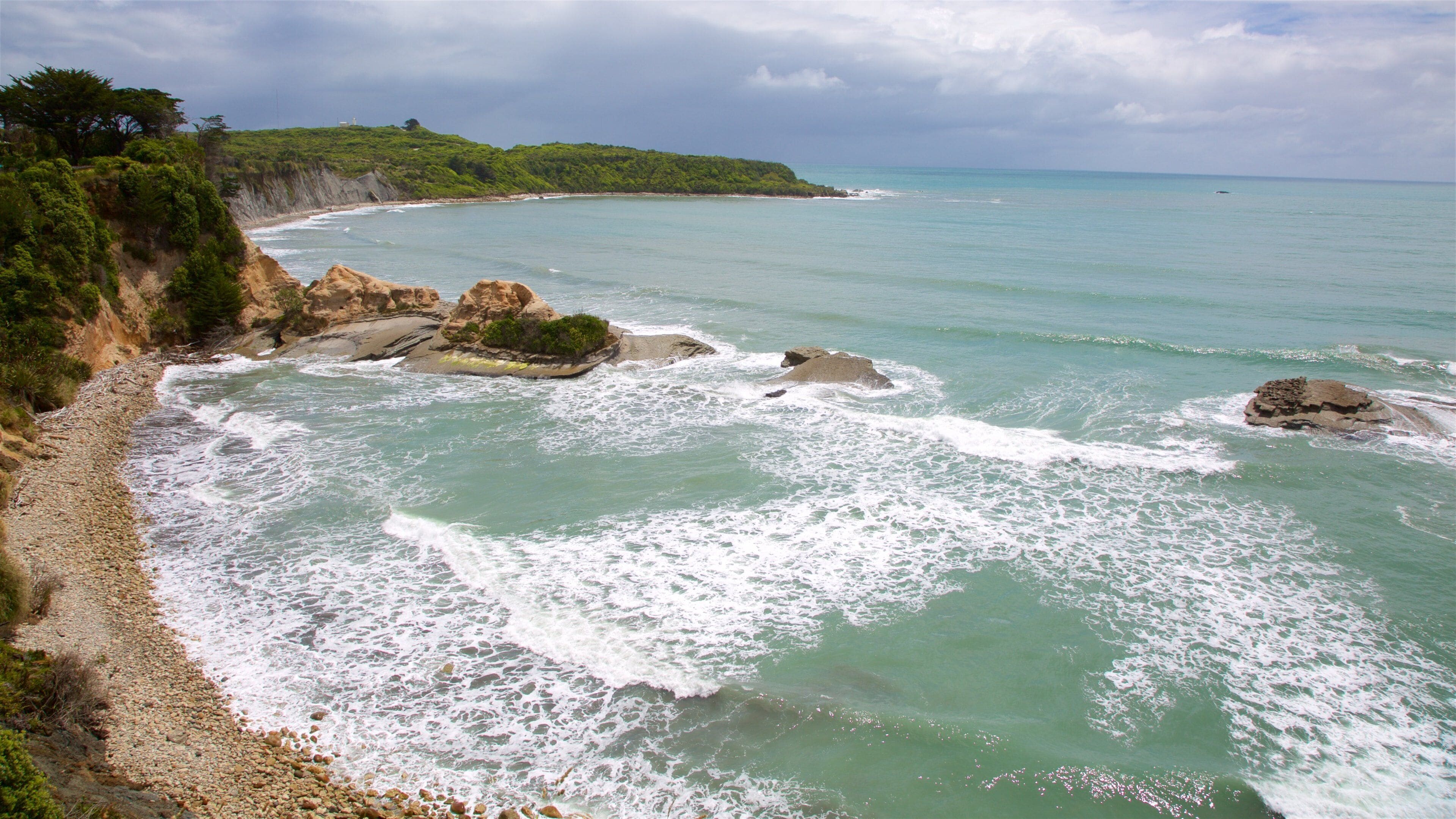 A coastal landscape with rocky outcrops, a sandy beach, and a green hillside.