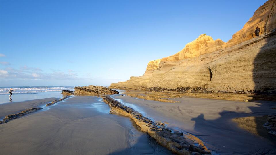 A coastal landscape with layered rock formations and a beach.