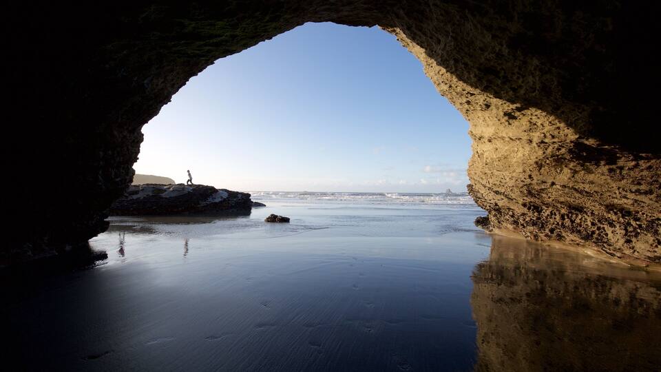 A beach through a natural rock arch with waves in the background.