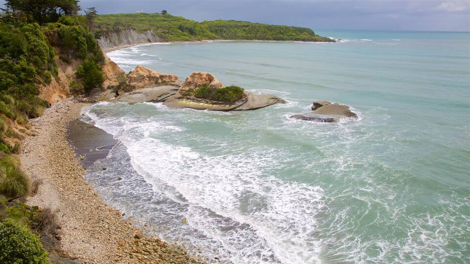 A coastal landscape with rocky outcrops, a sandy beach, and a clear view of the ocean.