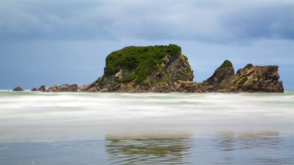 A rocky island with lush green vegetation surrounded by calm ocean waves.