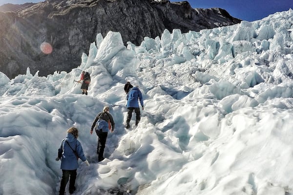 Um grupo de pessoas caminhando em uma montanha coberta de neve, com um afloramento rochoso ao fundo.