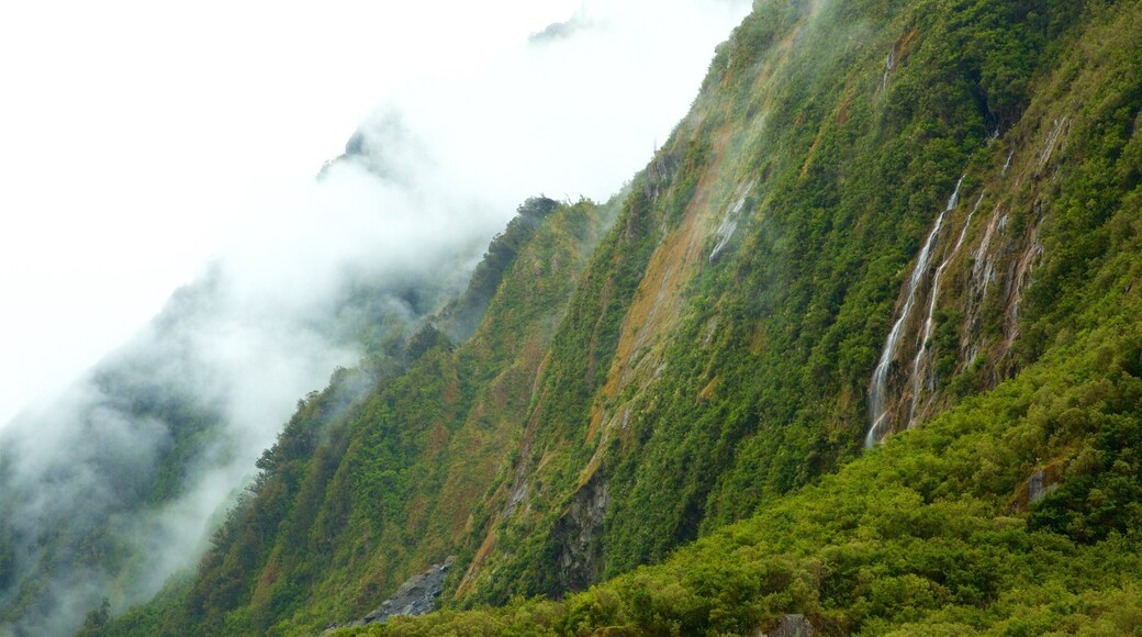 Fox Glacier ofreciendo montañas, una cascada y neblina o niebla