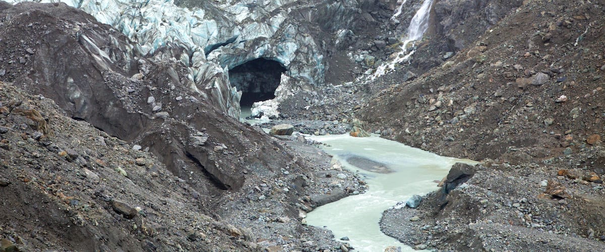 A glacier with a river flowing through a rocky canyon.