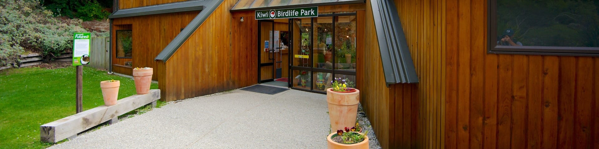 Un bâtiment en bois avec une enseigne indiquant « Kiwi Birdlife Park », et un chemin de gravier menant à l’entrée.