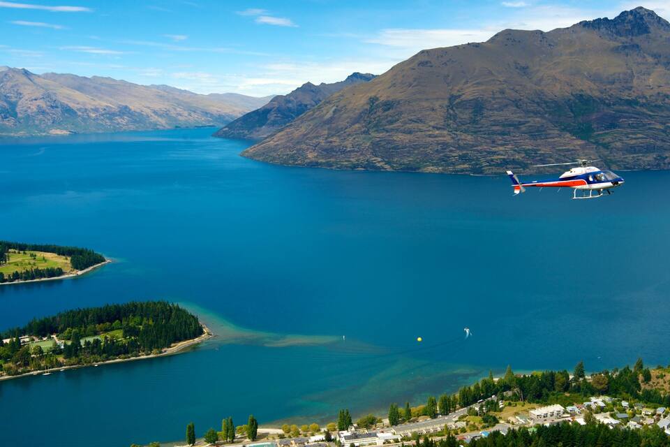 A helicopter flying over a large lake with mountains in the background.