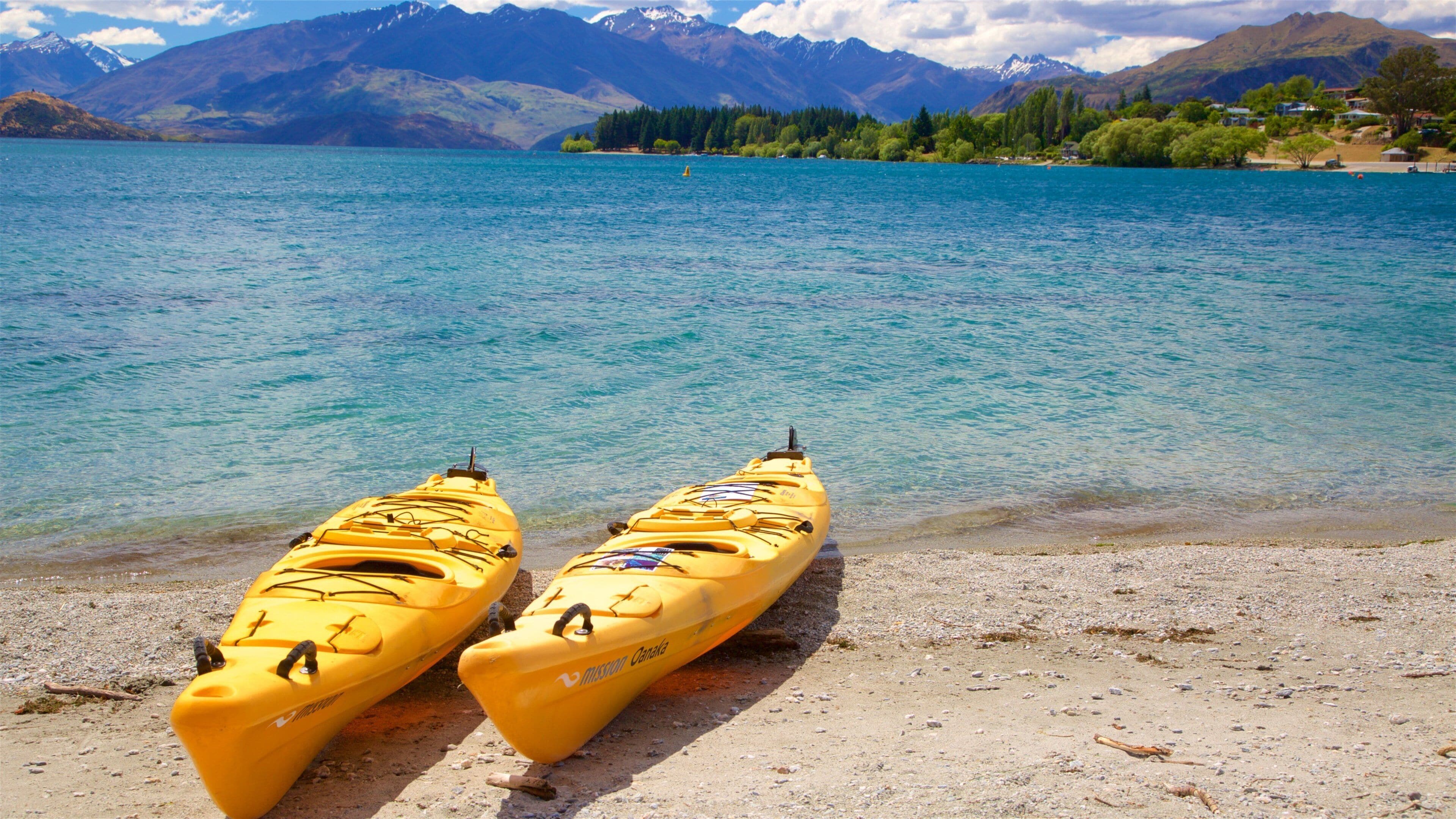 Two yellow kayaks on a pebbly shore with a lake and mountains in the background.