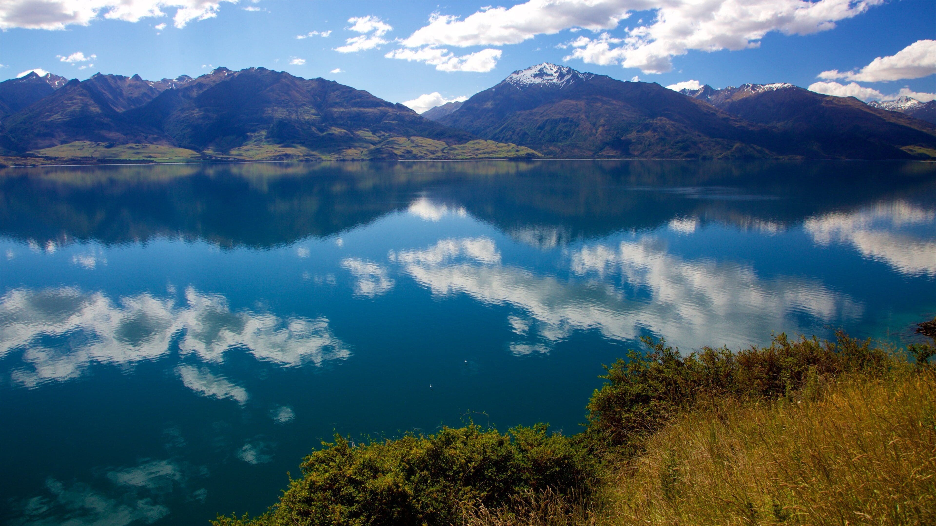 A calm lake with clear reflections of the sky and mountains in the background.