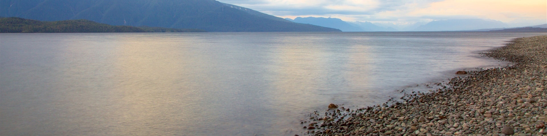 Lake Te Anau featuring a sunset, a pebble beach and mountains