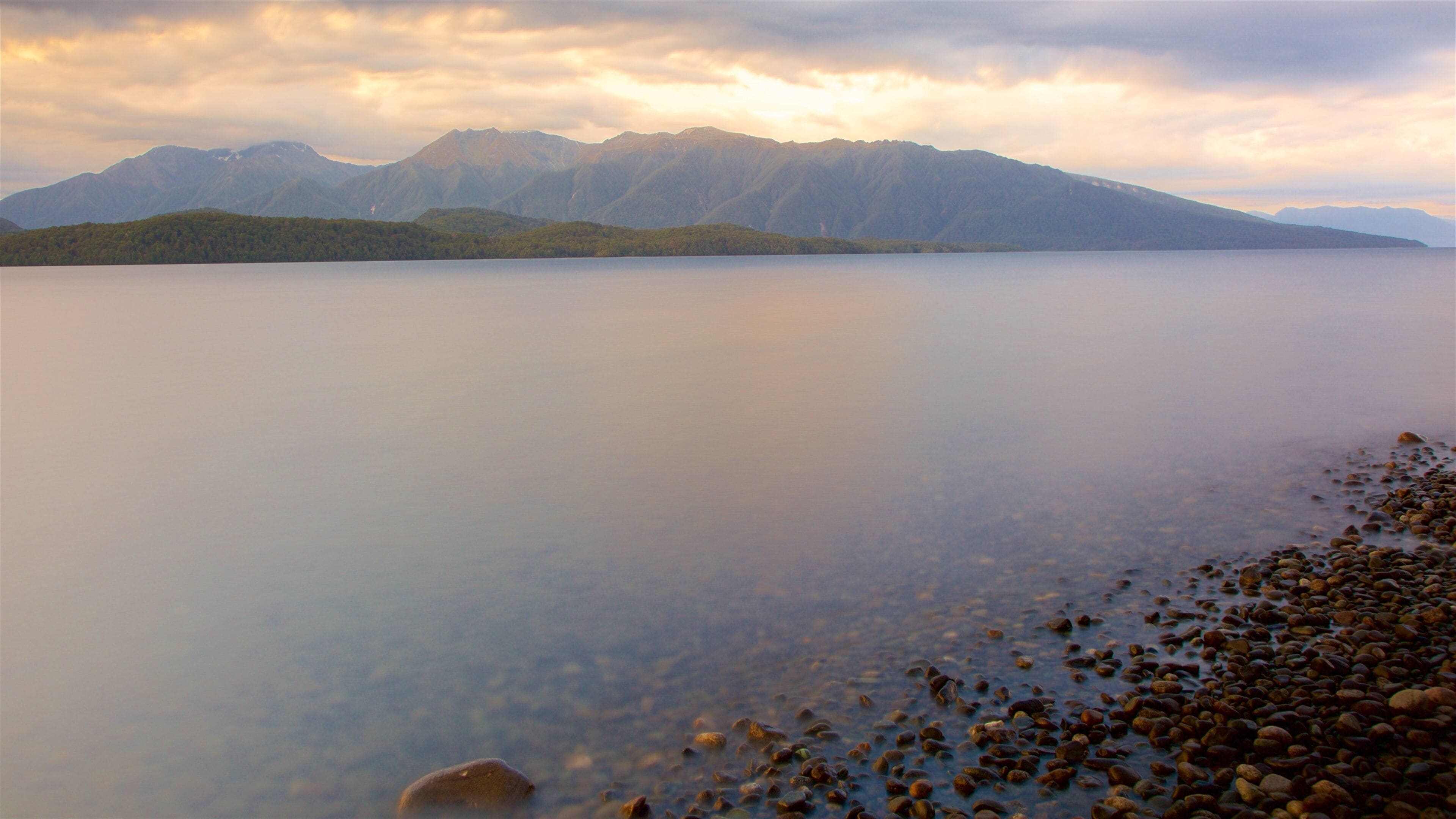 Lake Te Anau which includes a sunset, mountains and a lake or waterhole