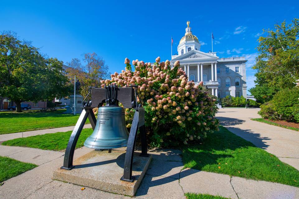 A large bell in front of a grand building with a dome and columns.