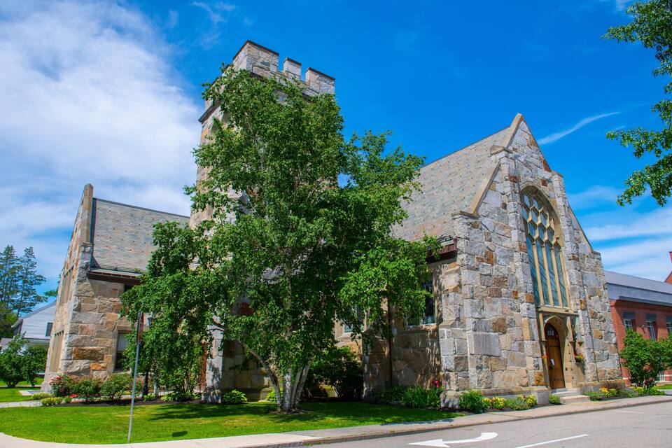 A stone church with a large tree in front.