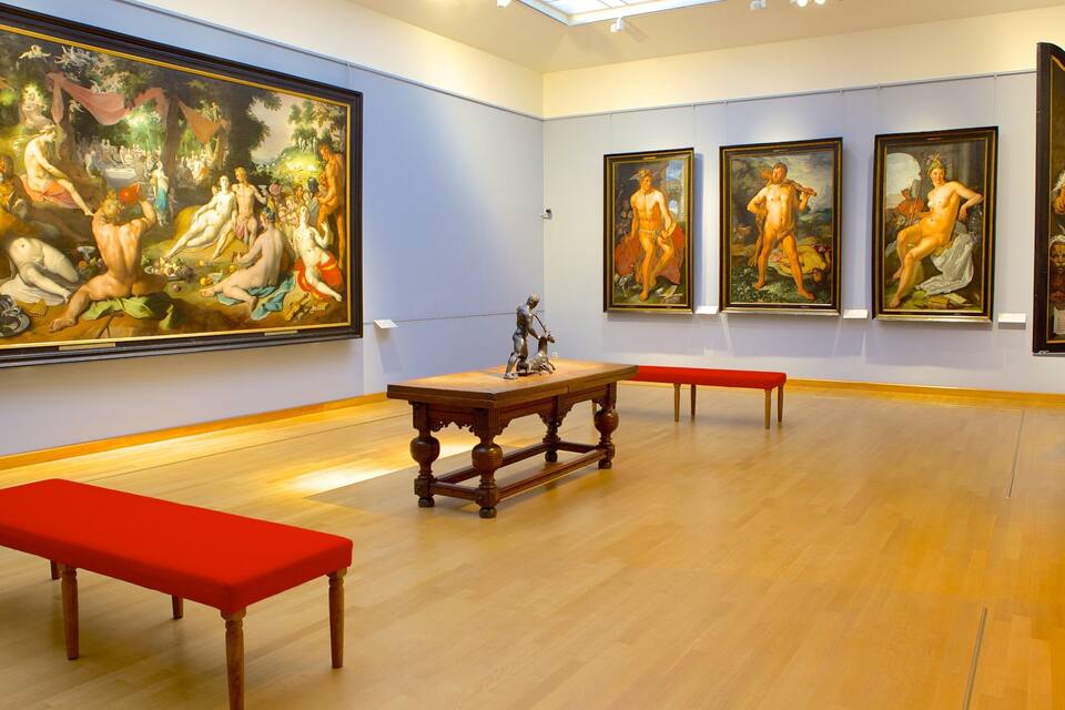 Una galería de arte con pinturas clásicas, bancos de madera y una gran escultura.
