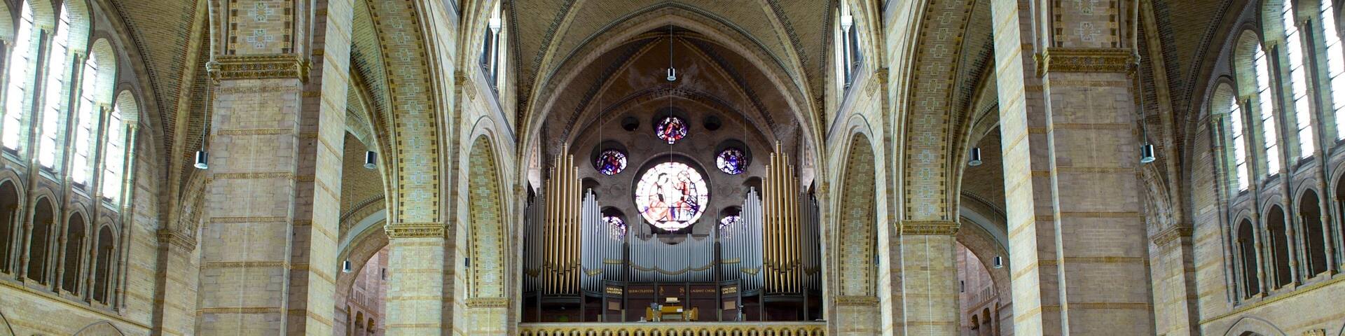A cathedral interior with high vaulted ceilings, rows of pews, and stained glass windows.