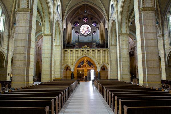 L’intérieur d’une cathédrale, avec de hauts plafonds en voûte, des rangées de bancs et des vitraux.