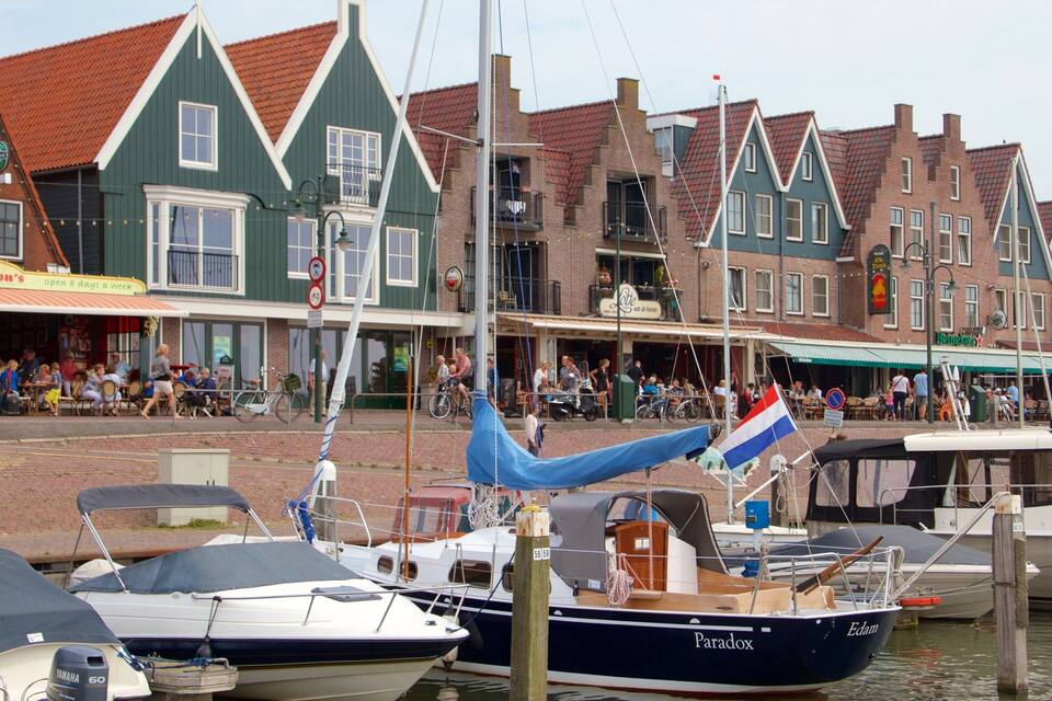 Un port où sont amarrés des bateaux, un drapeau néerlandais et des bâtiments européens traditionnels aux toits rouges.