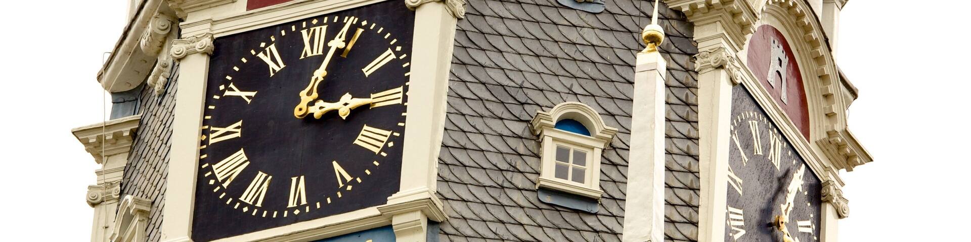 A clock tower with ornate architectural details and a sign that reads "Singulas Horas Singulas Vitasputa".
