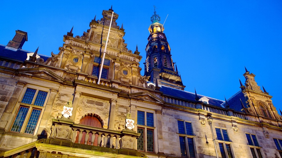 Un edificio histórico con arquitectura ornamentada, una destacada torre del reloj y una estatua en el balcón.