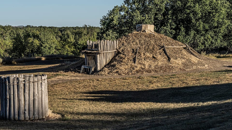 A dry, grassy field with a wooden fence, a pile of dirt, and a small structure covered with a tarp.