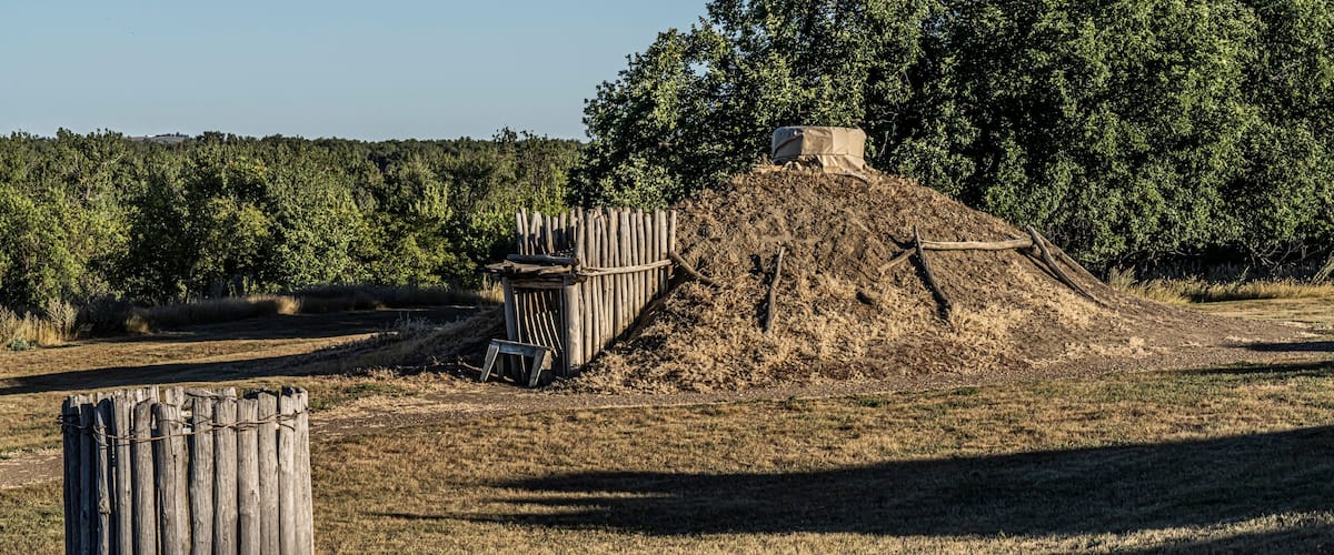 A dry, grassy field with a wooden fence, a pile of dirt, and a small structure covered with a tarp.