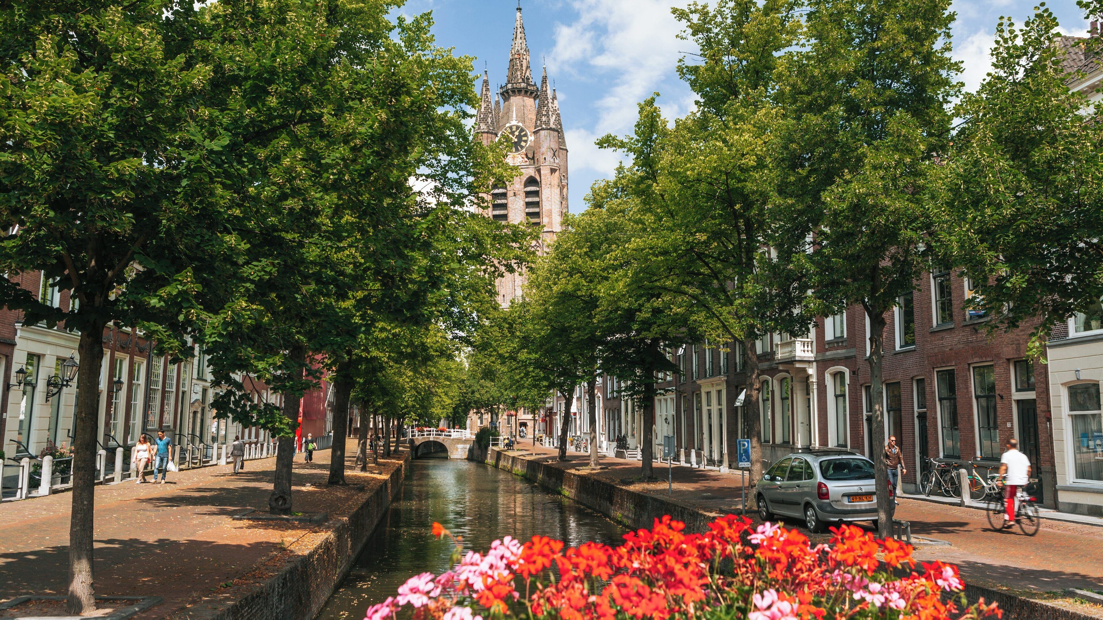 Oude Kerk stands majestically in Delft, South Holland, surrounded by vibrant flowers and historic canals under a blue sky