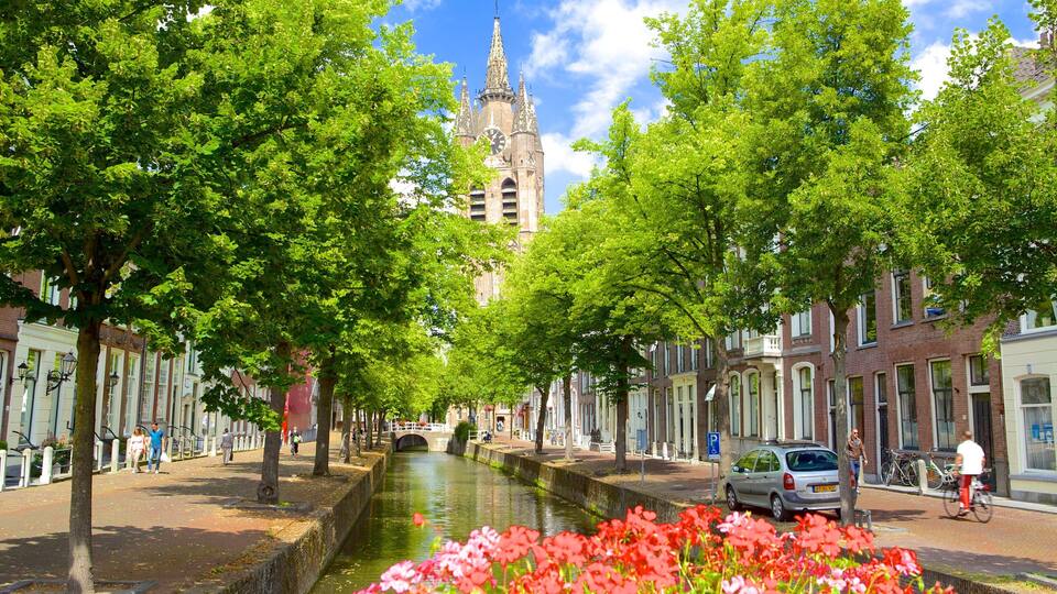A canal with a bridge, lined with trees and buildings, and a tower in the background.