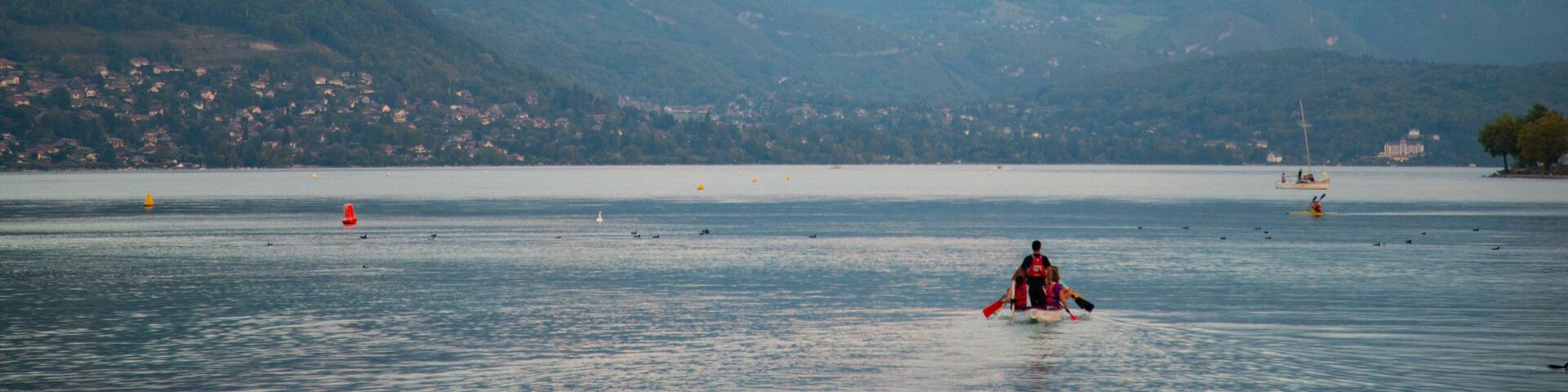 A lake with mountains in the background, a small boat with people, and several buoys.