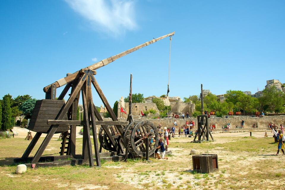 A historical reenactment site with wooden siege engines and a stone fortification.