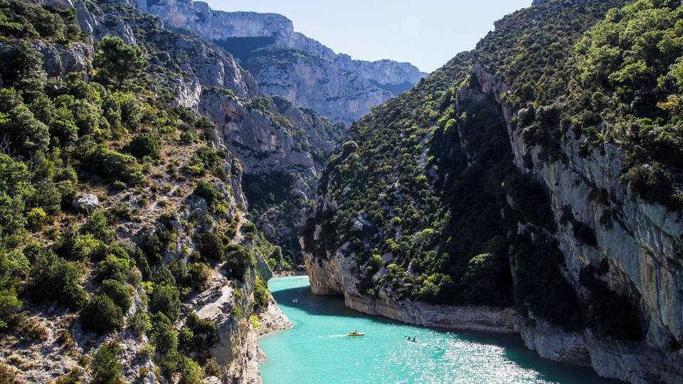 A canyon with turquoise water, rocky cliffs, and sparse vegetation.