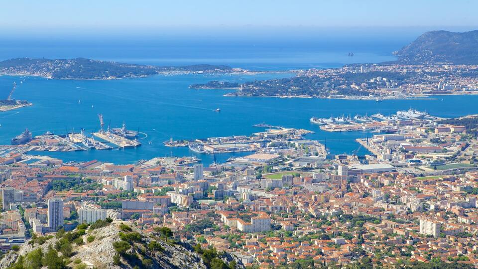 A coastal city with a harbor, ships, and a mountainous backdrop.