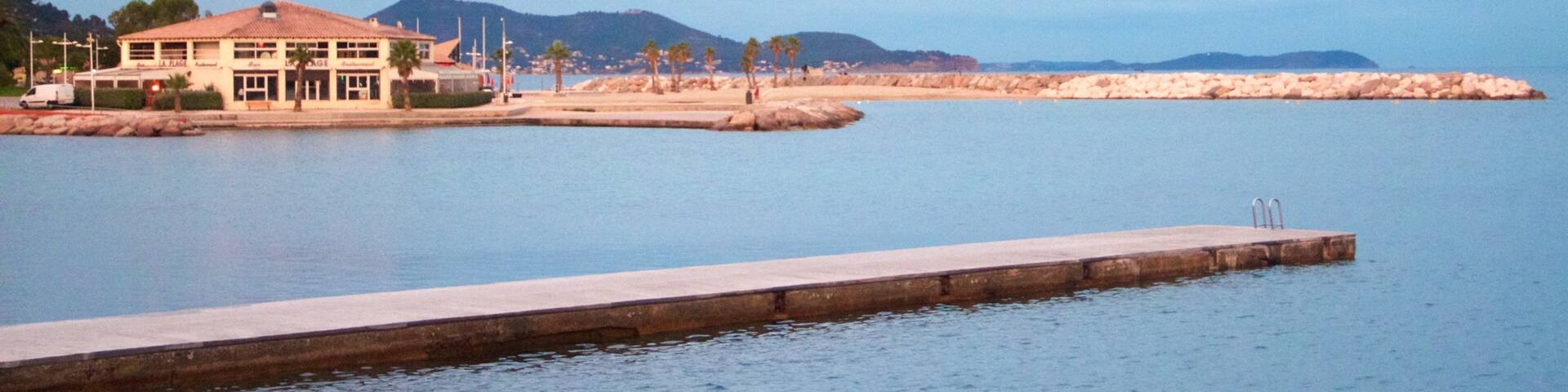 A waterfront property with a pool, a pier, and a beach in the background.